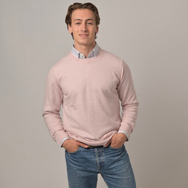 Männermodel trägt klassischen Herren-Kaschmirpullover mit Rundhalsausschnitt in Hellrosa aus 100 % Kaschmir zu Hemd und Jeans