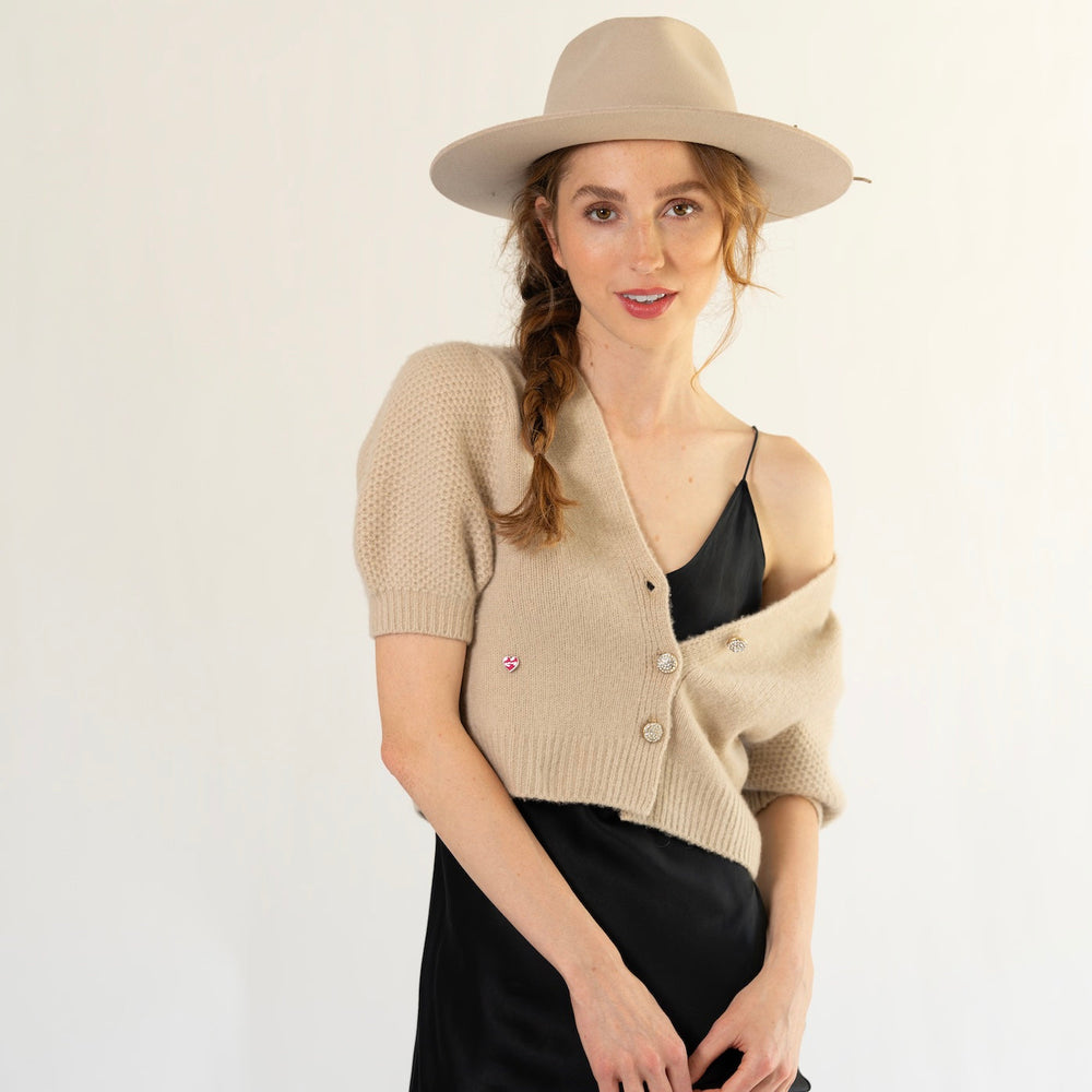 Model trägt das Kaschmir Cardigan Leni‑cs von cute stuff mit V‑Ausschnitt und kurzen Ballonärmeln aus 100% reinem Kaschmir in der Beige über einem Abendkleid