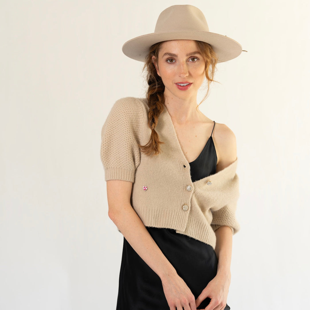 Model trägt das Kaschmir Cardigan Leni‑cs von cute stuff mit V‑Ausschnitt und kurzen Ballonärmeln aus 100% reinem Kaschmir in der Beige über einem Abendkleid